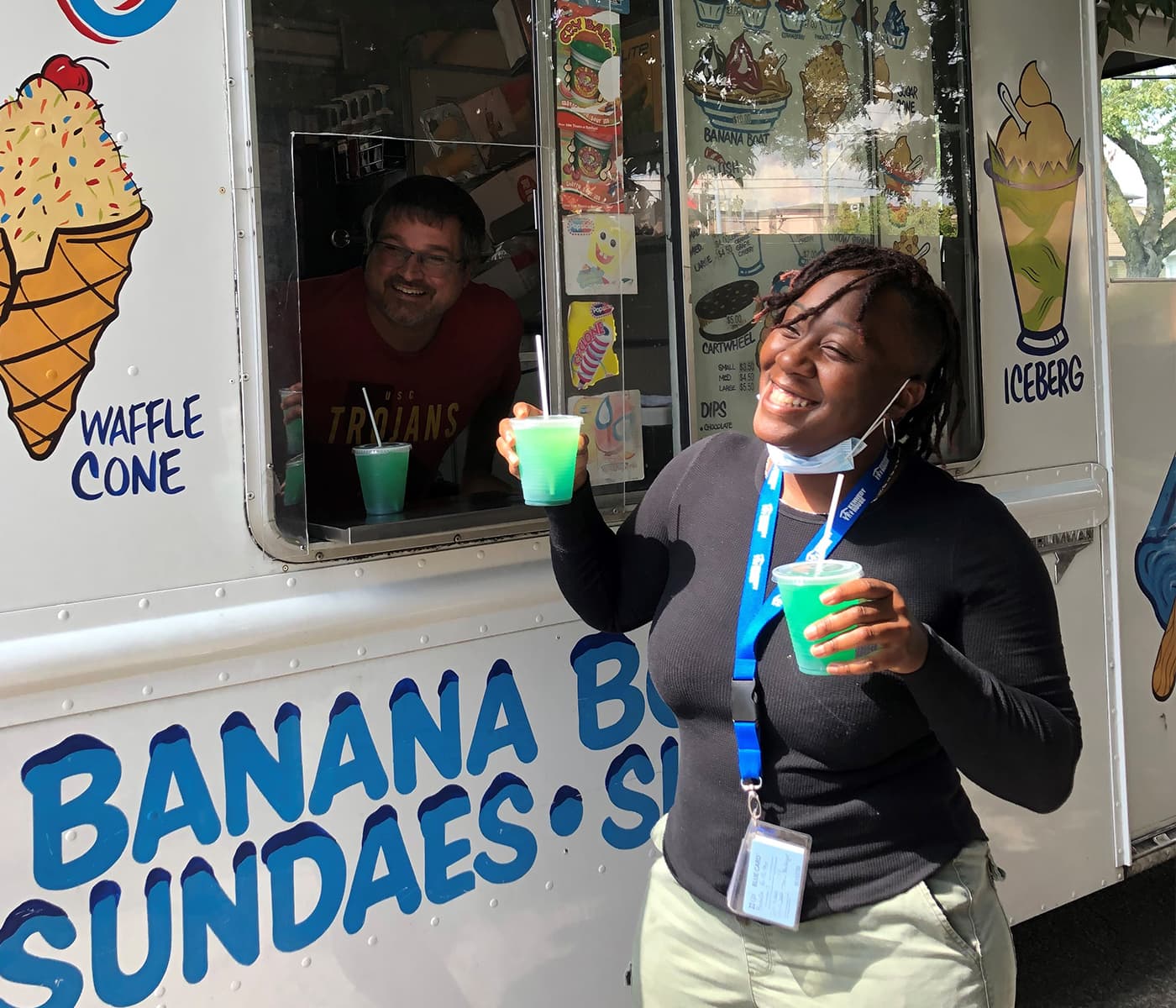 A woman holding two slushies smiling with the ice cream man