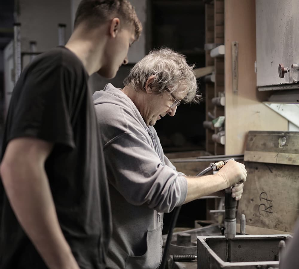 An older gentlemen showing a younger person how to work with power tools