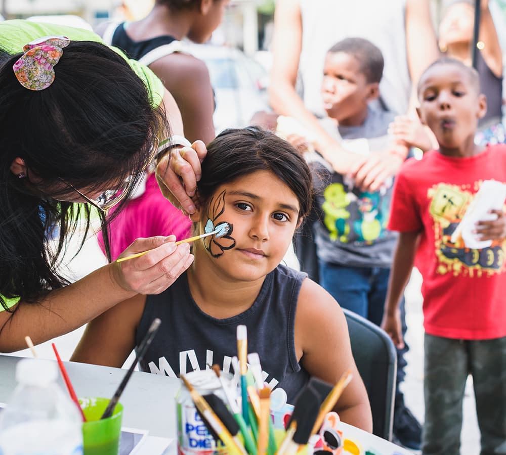 A child getting a flower painted on her cheek