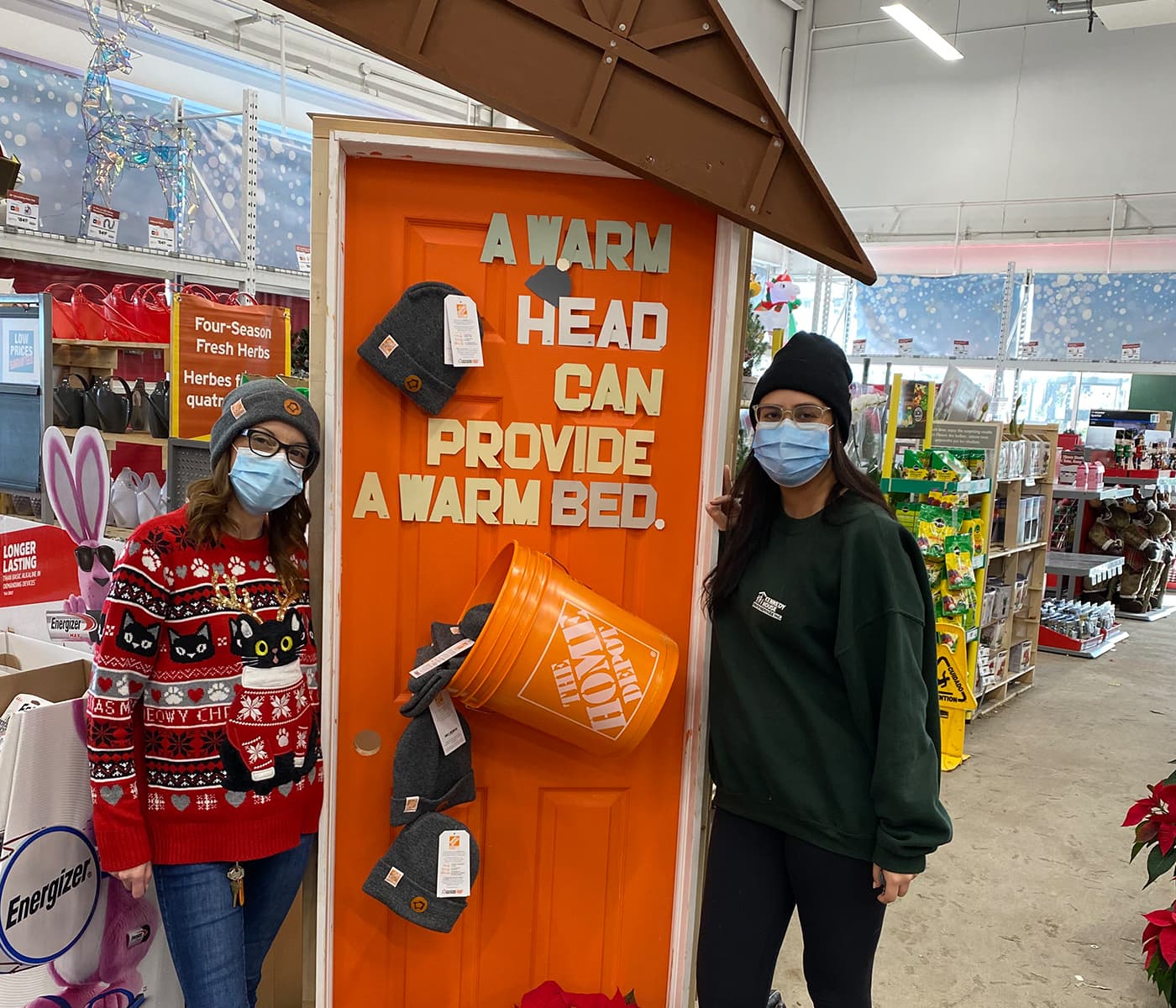 Two women standing in front of an orange door that says "A warm head can provide a warm bed"
