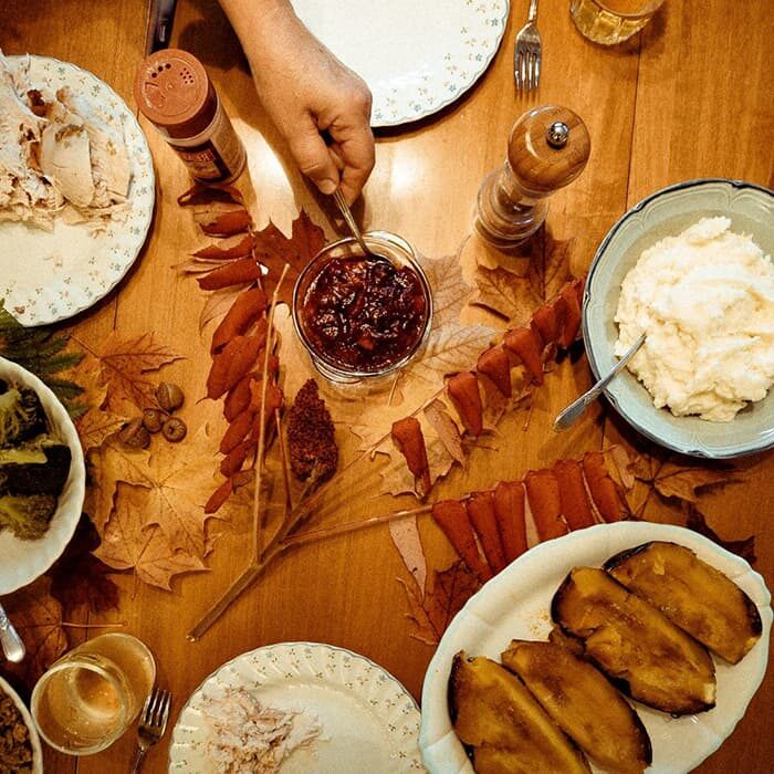 A hand reaching for cranberry sauce on a table with a holiday feast on it