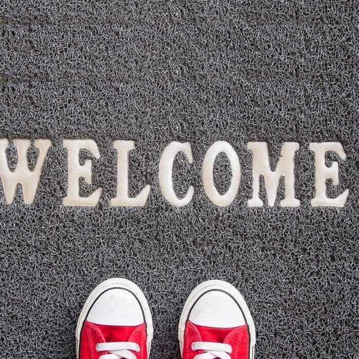A youth with red sneakers standing on a grey floor mat that says "Welcome"says